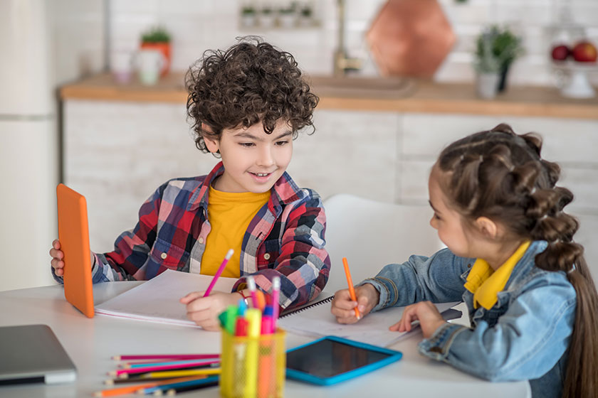 Curly boy and dark-haired girl sitting at table with tablets