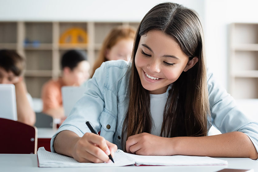 Smiling schoolgirl writing on notebook in classroom