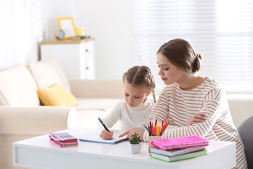 Woman helping her daughter with homework at table